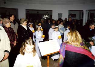 Dziewczynki oraz chłopcy ubrani na biało za roratką wchodzą do świątynini z lampami